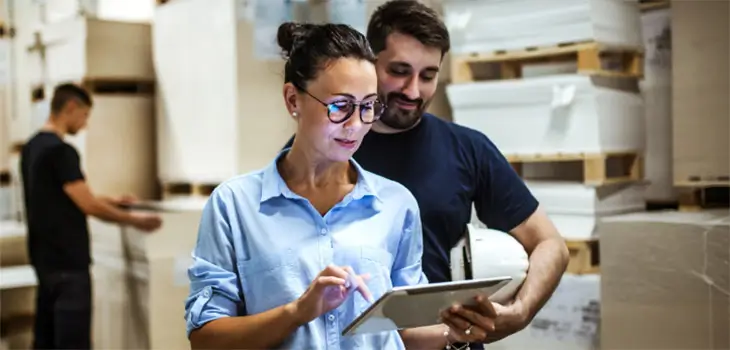 Business couple in warehouse looking at tablet.