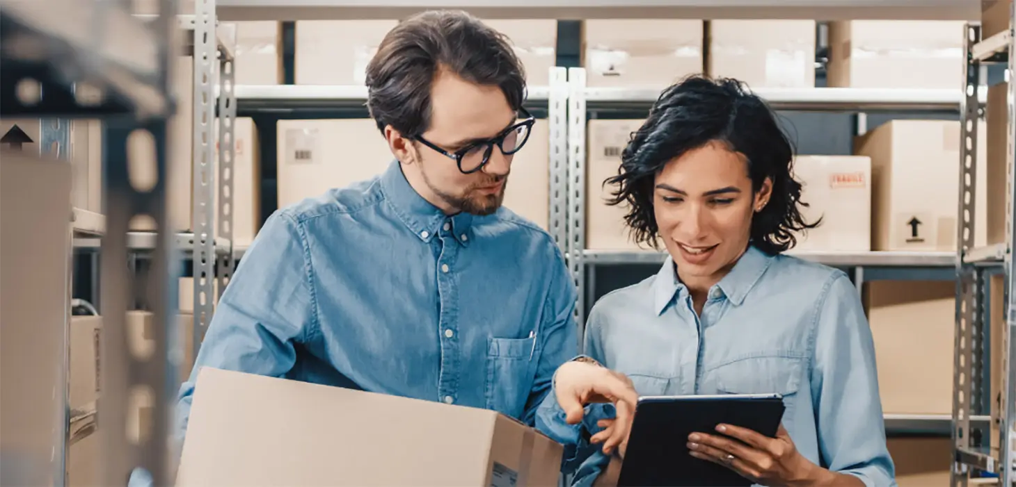 Two business colleagues check inventory on tablet in warehouse