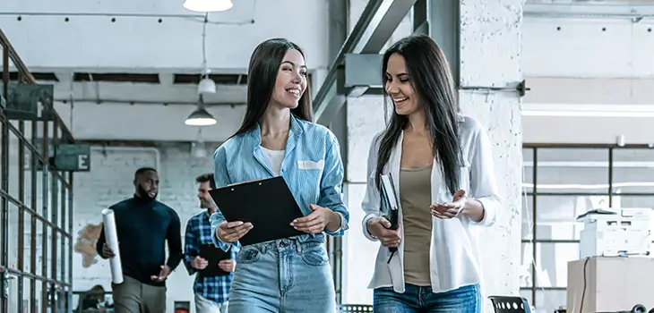 Two female colleagues smiling as they walk through modern office